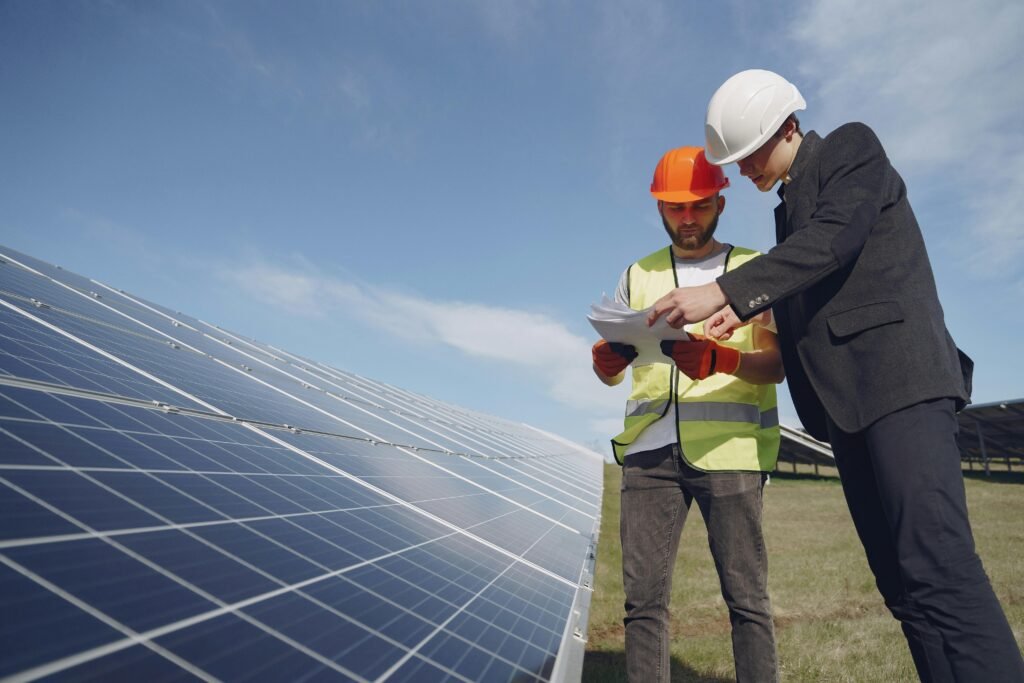 Low angle of young inspector and foreman in hardhats checking documentation against modern solar panels in field