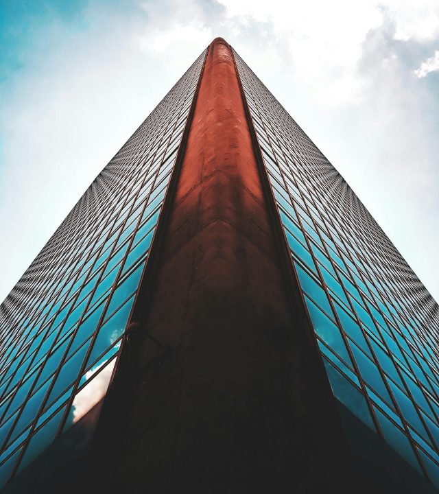 Striking low angle view of a modern skyscraper with reflective glass windows against a blue sky.