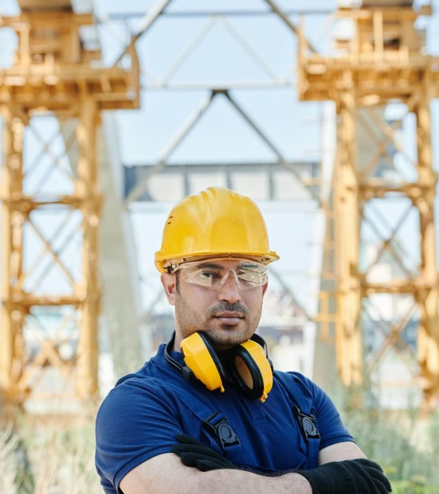 Confident engineer standing with protective gear at a construction site.